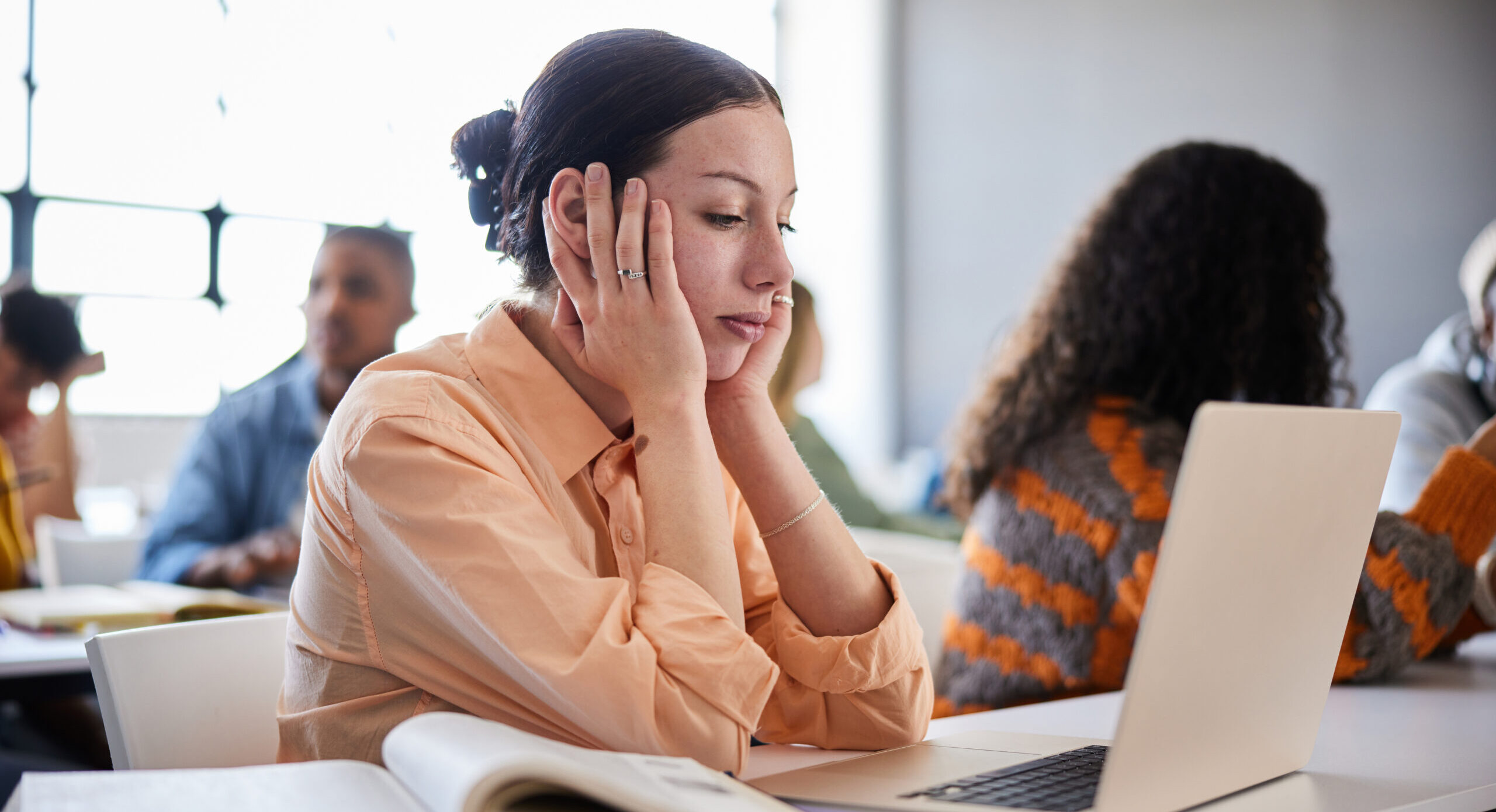 Junge Frau sitzt am Laptop und wirkt abgelenkt – symbolische Darstellung von Konzentrationsproblemen bei ADHS.